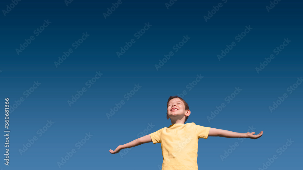 Happy smiling 5-year-old Caucasian boy with closed eyes and upturned face in yellow t-shirt with outstretched arms im summer with blue sky gradient on background. Horizontal banner, large copy space. Happy smiling 5-year-old Caucasian boy with closed eyes and upturned face in yellow t-shirt with outstretched arms im summer with blue sky gradient on background. Horizontal banner, large copy space.