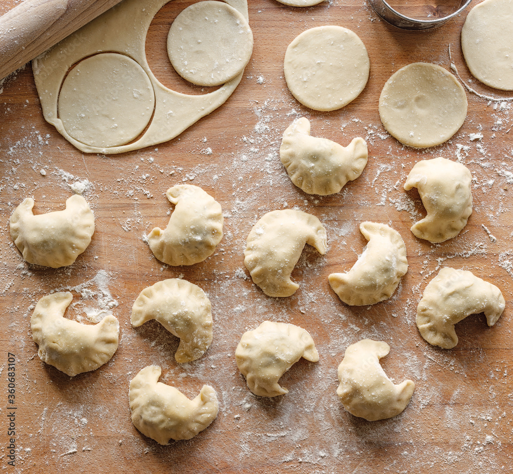 Raw dumplings with mushroom and lentils filling prepared for cooking on a wooden board, top view
