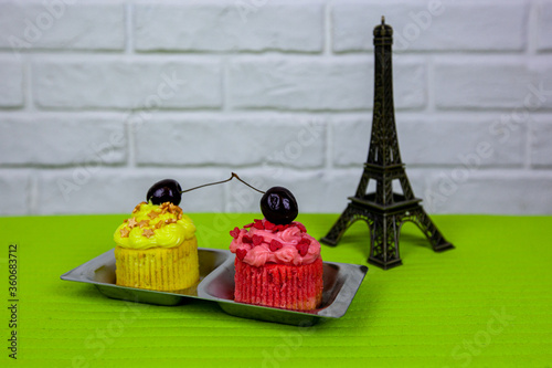 Two pink and yellow cupcakes with cherries and Eiffel Tower figurine nearby. photo