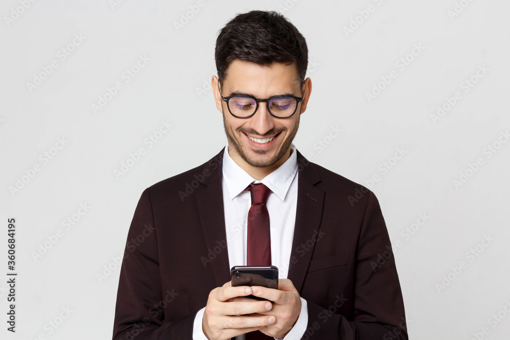 Young business man dressed in maroon suit, looking at screen of phone he is holding, reading messages, isolated on gray background Young business man dressed in maroon suit, looking at screen of phone he is holding, reading messages, isolated on gray background