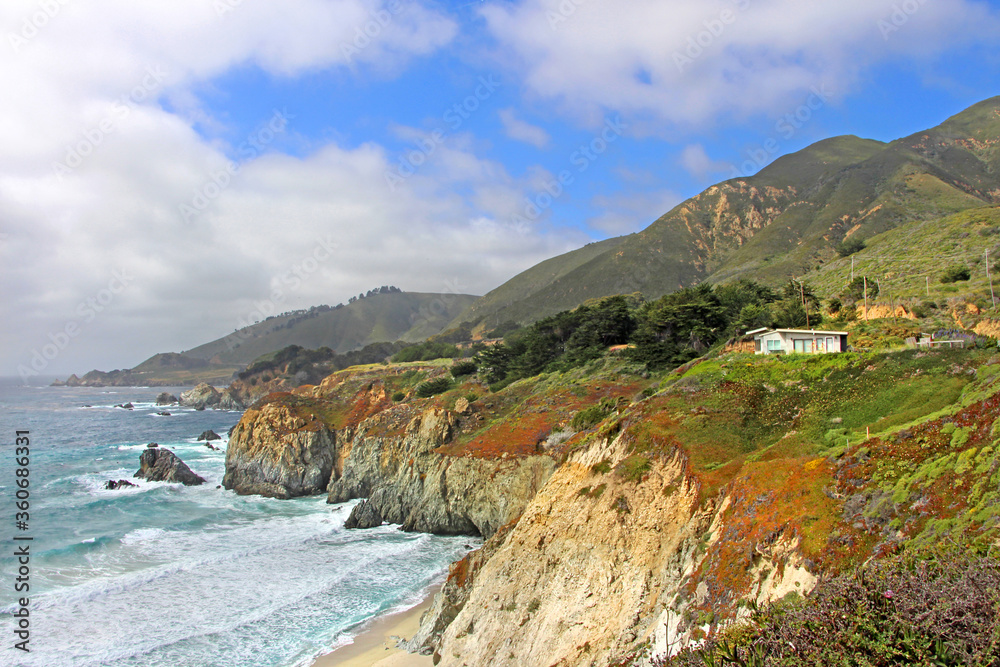 Beautiful shore / coast of California scenic drive near Big Sur. The view on the white sand beach, turquoise sea and green / red plants covering high rocky cliffs and hills. 