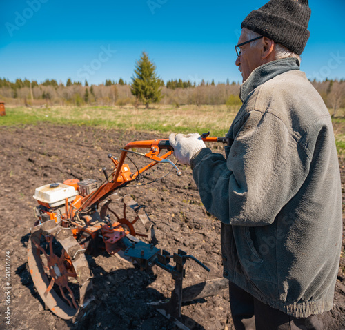 an elderly man cultivates the land with a tillerblock photo