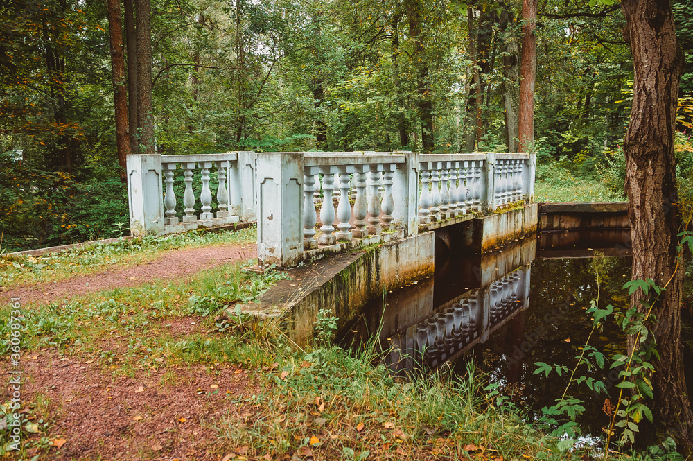 A small bridge with balusters over a stream in the forest. The architecture of the 19th century in the classicism style