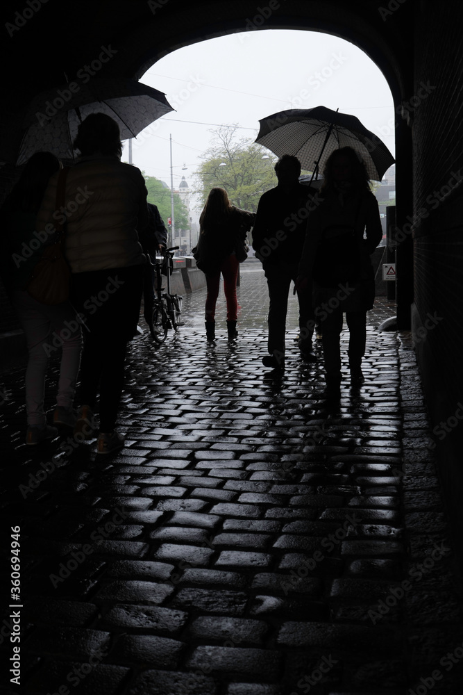 Unrecognizable people shelter from the rain with umbrellas in a stone archway at the Binnenhof in the city of The Hague, the Netherlands