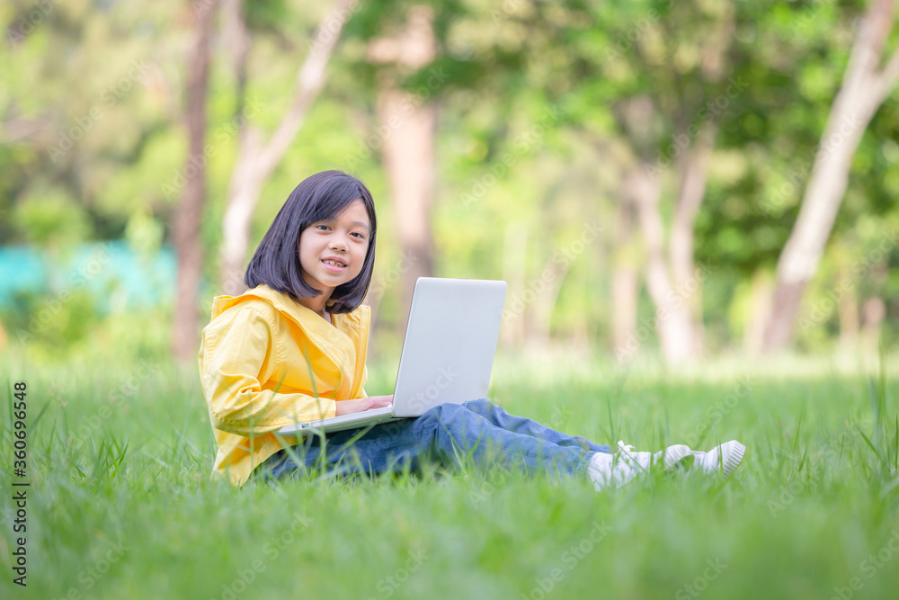 Smiling girl sitting on the grass studying with laptop in the park, Outdoor learning concept Smiling girl sitting on the grass studying with laptop in the park, Outdoor learning concept