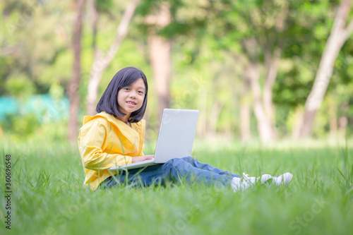 Smiling girl sitting on the grass studying with laptop in the park, Outdoor learning concept