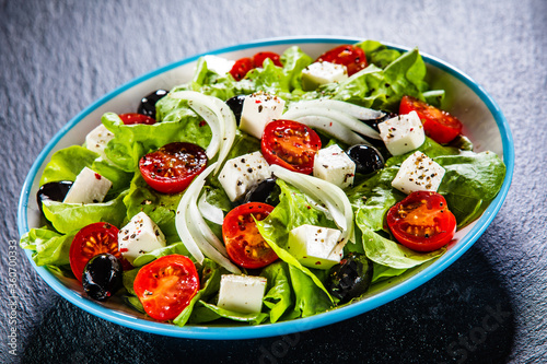 Fresh Greek salad - feta cheese, cherry tomatoes, lettuce, black olives and onion on black stone board
