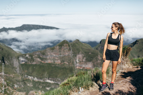 Happy athletic girl in tracksuit at the peak of the mountain looks away. Beautiful fit figure, tanned body
