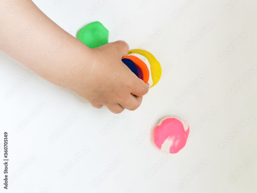 Toddler sculpts from colored plasticine on a white table. The hand of a small child squeezes pieces of colored plasticine. Children's creativity, educational games, fine motor skills. Top view. Toddler sculpts from colored plasticine on a white table. The hand of a small child squeezes pieces of colored plasticine. Children's creativity, educational games, fine motor skills. Top view.