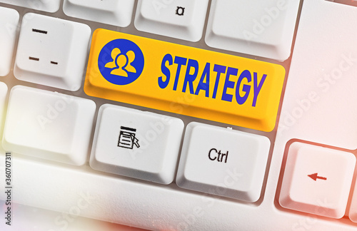 Conceptual hand writing showing Strategy. Concept meaning action plan or strategy designed to achieve an overall goal White pc keyboard with empty note paper above white key copy space photo