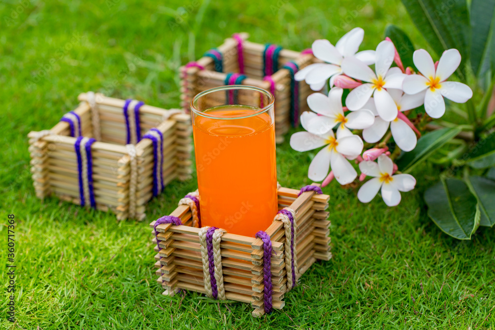 Bamboo sticks glass holder with a glass of orange juice on grass background. Bamboo sticks glass holder with a glass of orange juice on grass background.