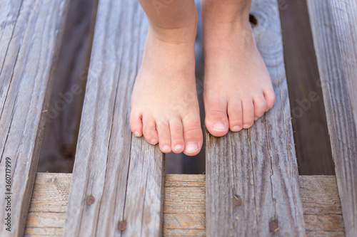 Kids legs of a small child standing on a wooden floor near pool during summer vacation. Selective focus.