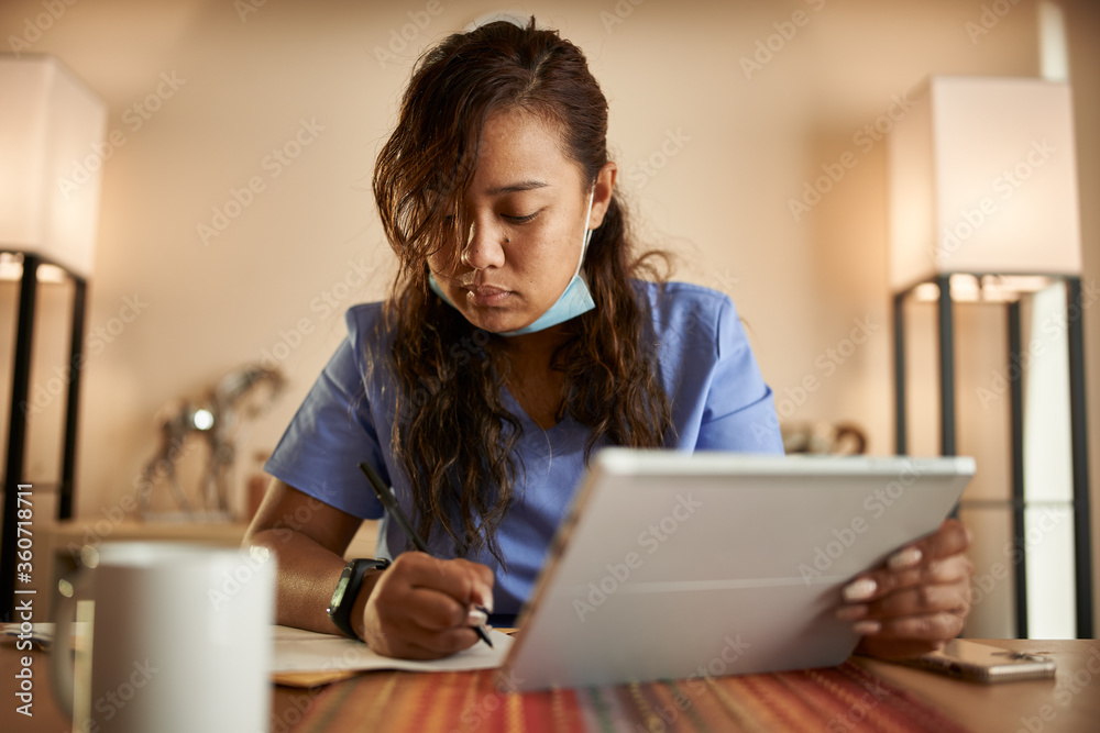 filipina nurse working from home doing paperwork and using tablet filipina nurse working from home doing paperwork and using tablet