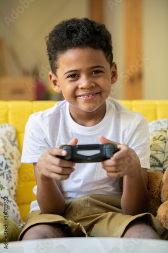 Cheerful little boy of African ethnicity with joystick looking at you with smile