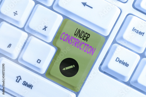 Conceptual hand writing showing Under Construction. Concept meaning building that is unfinished but actively being worked on White pc keyboard with empty note paper above white key copy space