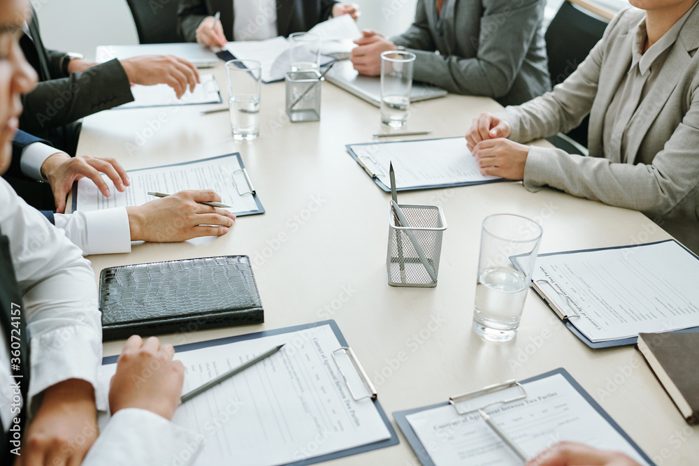 Group of business partners or colleagues reading text of contract at meeting Group of business partners or colleagues reading text of contract at meeting