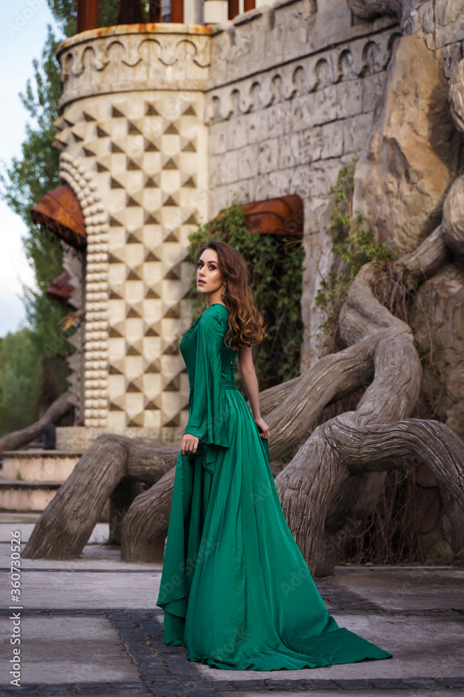 beautiful young woman in long green dress standing posing against the backdrop of a fairytale castle