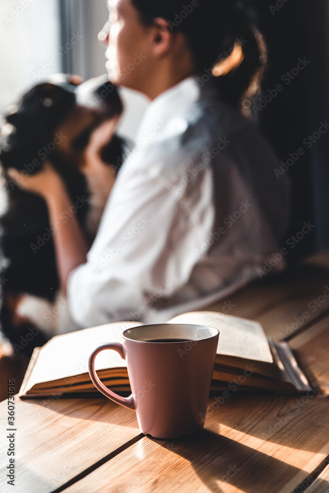 Yoman sitting in living room with her cute Bernese Mountain Dog dog, reading and drinking coffee. Yoman sitting in living room with her cute Bernese Mountain Dog dog, reading and drinking coffee.
