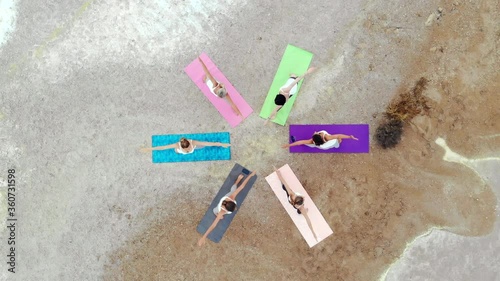 Drone point aerial view six yogi women wear activewear do yoga on nature near salt lake stand on mats in circle perform Extended Triangle (Utthita Trikonasana) asana. Yoga, healthy lifestyle concept