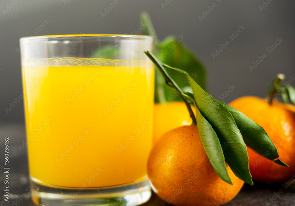 Fresh tangerine juice in a glass cup on a black background. Whole tangerines with green leaves lie nearby. Healthy eating concept Fresh tangerine juice in a glass cup on a black background. Whole tangerines with green leaves lie nearby. Healthy eating concept