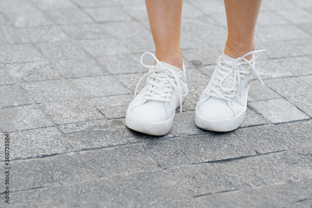 A person woman's legs in shoes standing on a sidewalk