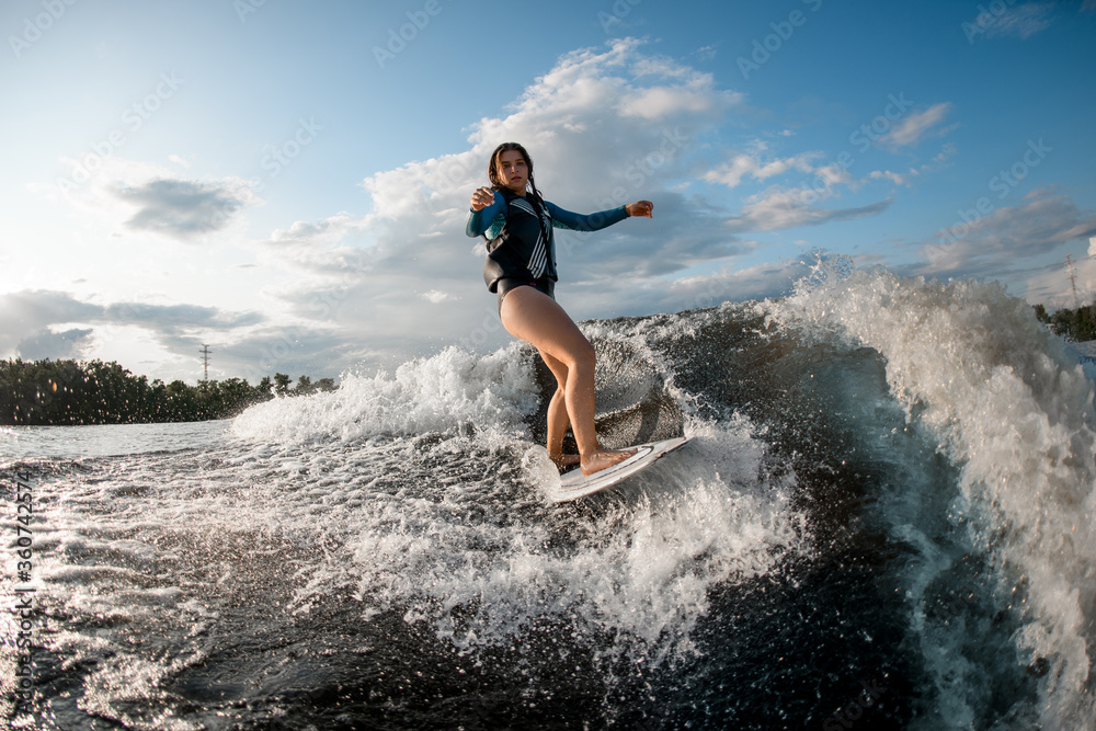 Active young woman wakesurfing down the river waves