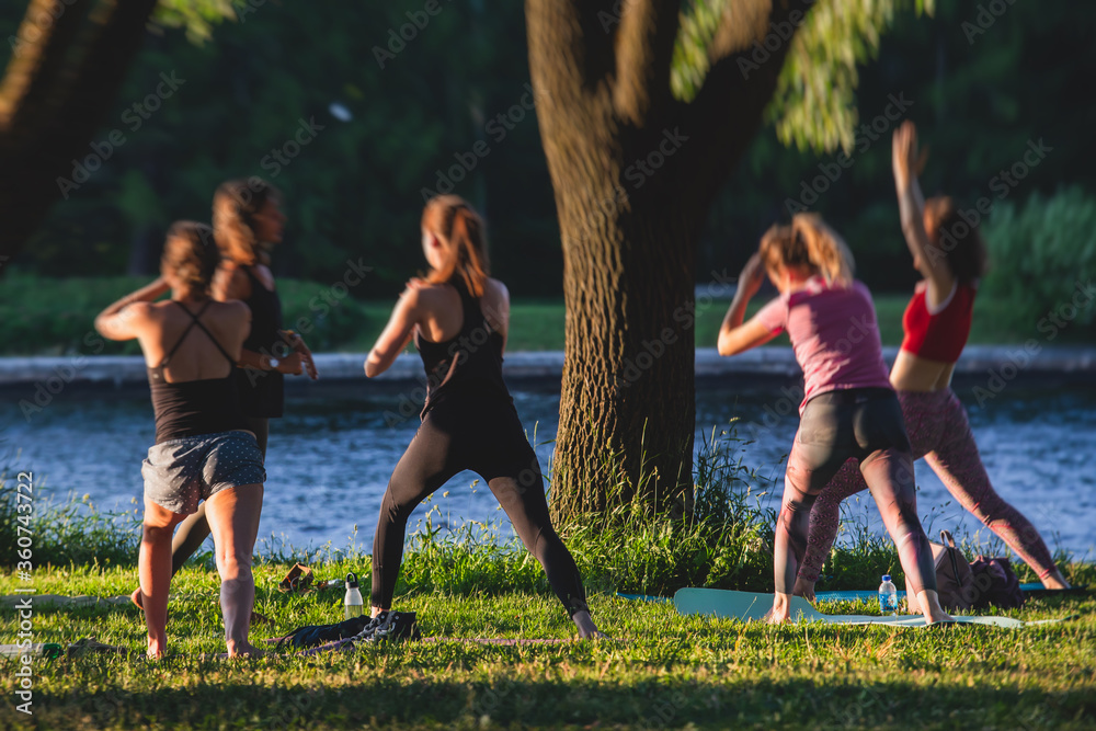 Group of women attending outdoor yoga class lesson, doing stretching workout together on the grass by the river. Group of women attending outdoor yoga class lesson, doing stretching workout together on the grass by the river.