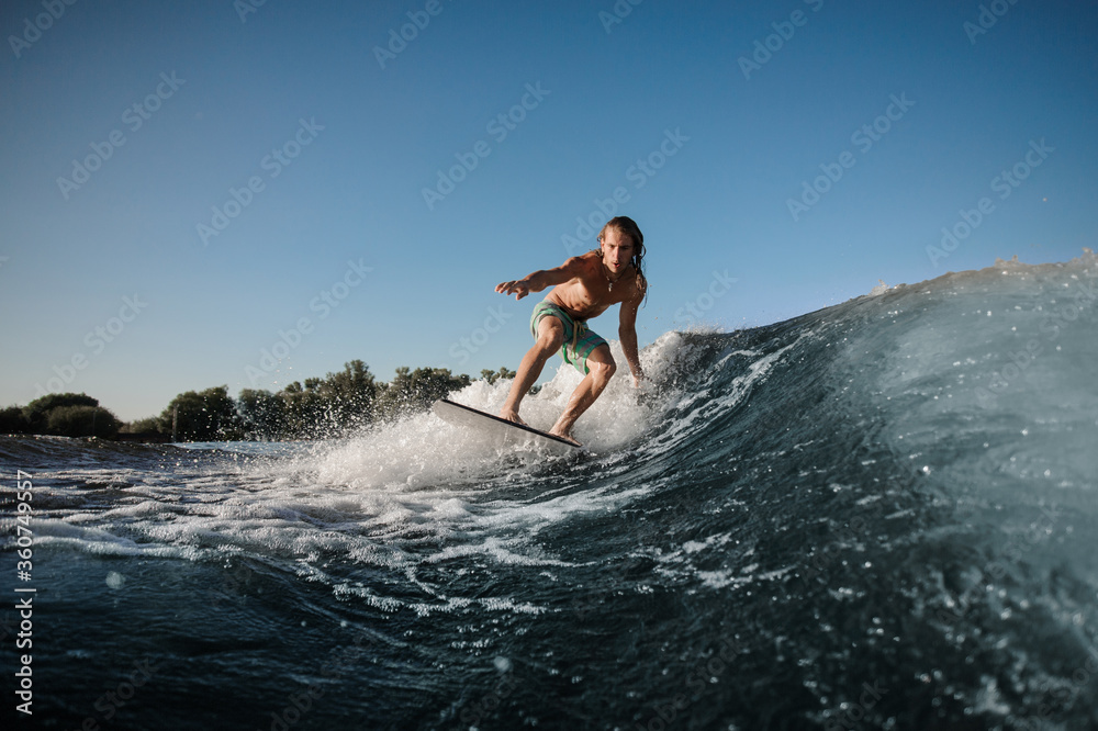 Active young man balancing on wake board down the river waves