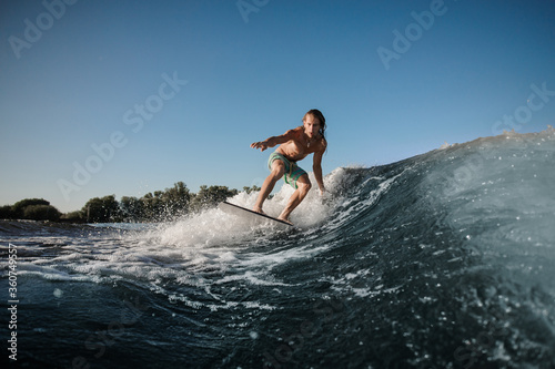 Active young man balancing on wake board down the river waves