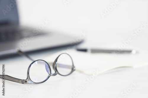 Eyeglasses, open notebook, pen and laptop on the office table. Top view with copy space. Selective focus image in business concept