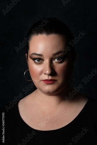 close up beautiful portrait of a plus size girl with a serious and strong facial expression on a black background