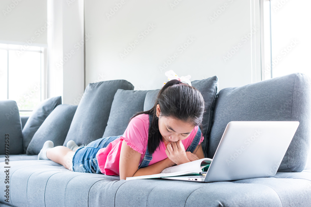asian girl learning from home with laptop and book on sofa in living room asian girl learning from home with laptop and book on sofa in living room