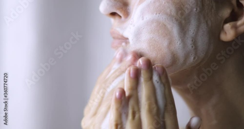 Woman is washing cleaning face with organic foamy soap cleanser, closeup view. Girl is cleansing her face skin, making massage movements. Beauty procedure, spa, wellness and healthy skin care concept.