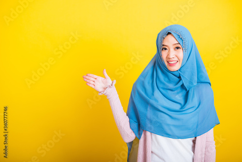 Asian Muslim Arab, Portrait of happy beautiful young woman Islam religious wear veil hijab funny smile she positive expression open palms with something on hand side space isolated yellow background © sorapop