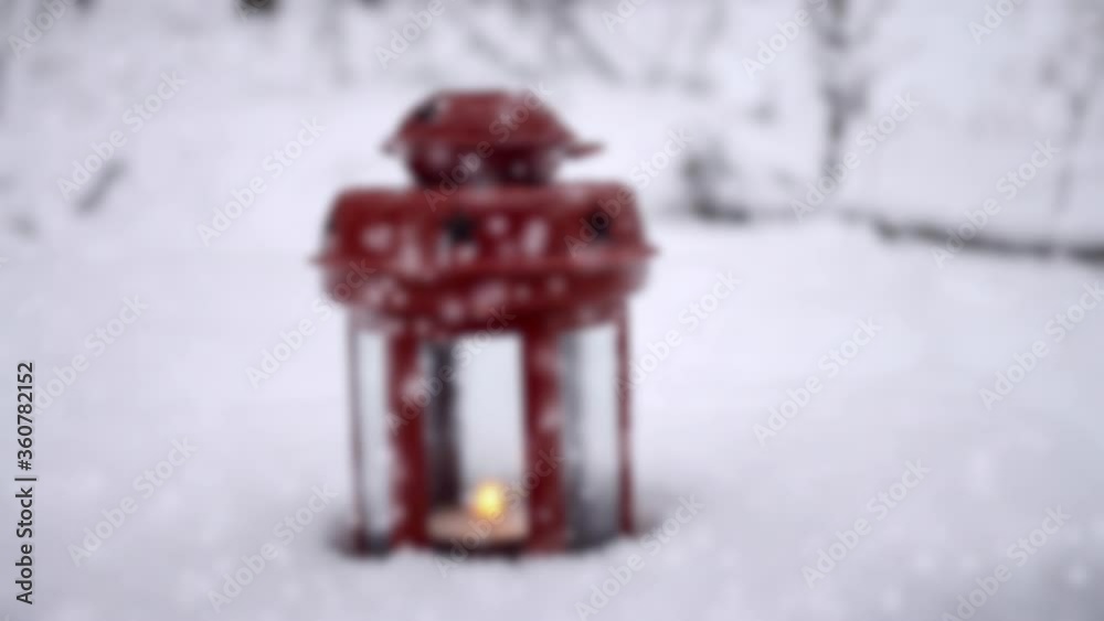 Red candle lantern with candle in snow during snowfall. Red candle lantern with candle in snow during snowfall.