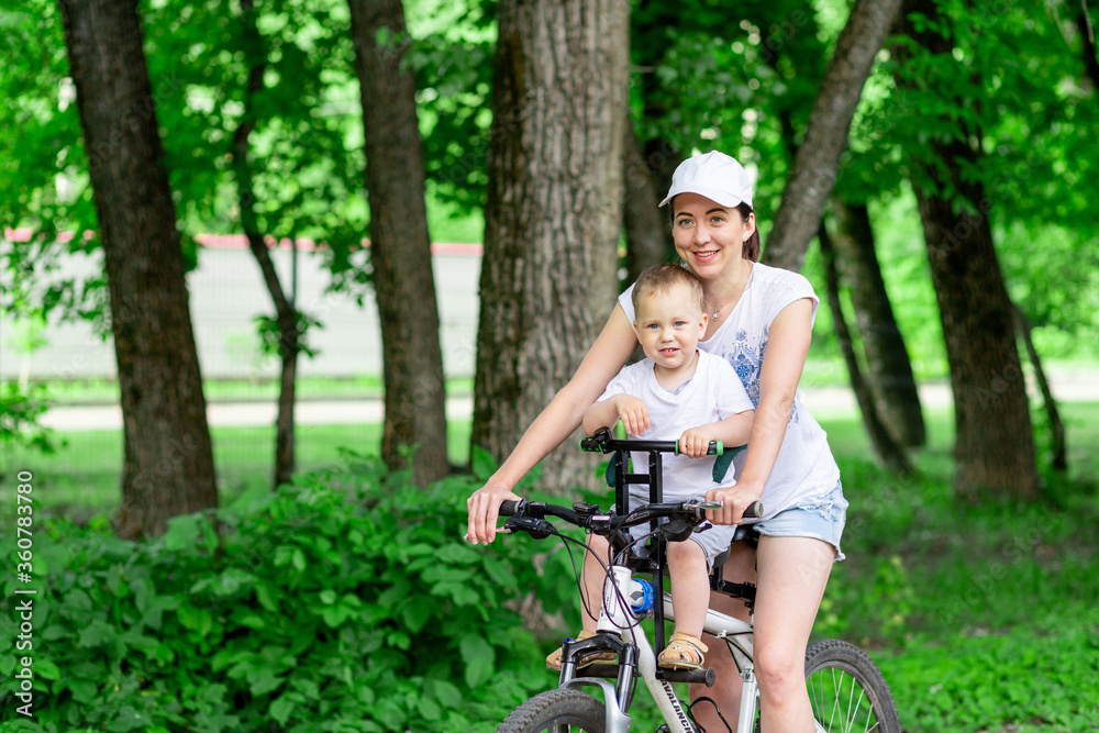 mother and son ride a Bicycle, mother carries a child in a child's chair on a Bicycle in the Park in the summer mother and son ride a Bicycle, mother carries a child in a child's chair on a Bicycle in the Park in the summer