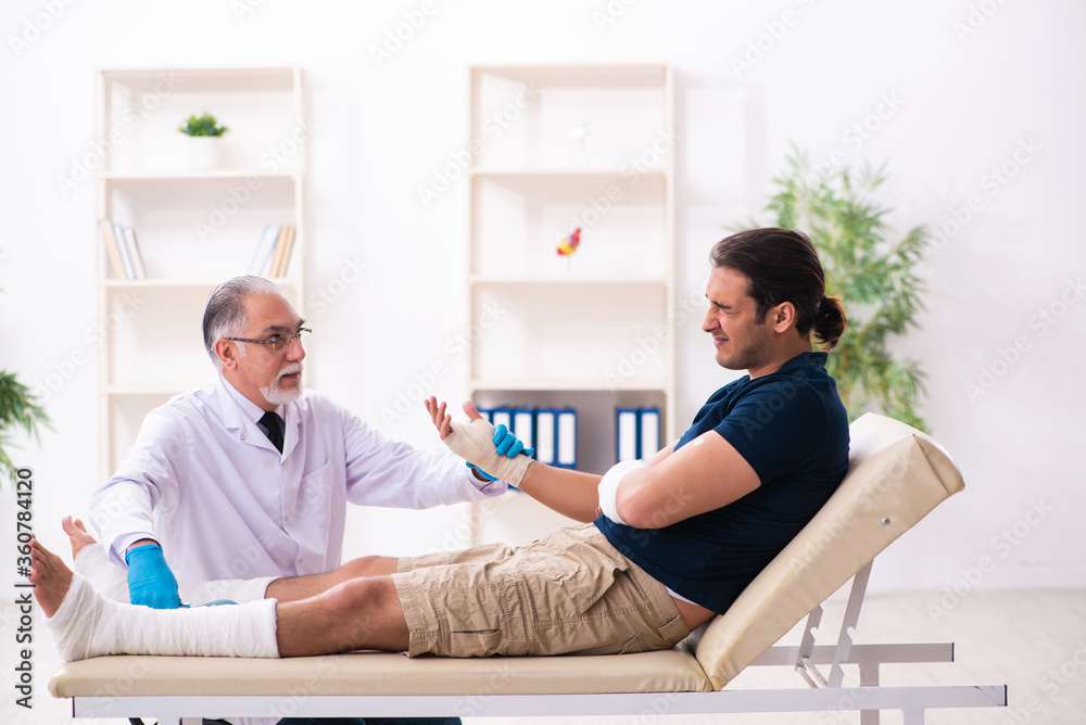 Fototapeta premium Young injured man visiting old doctor traumatologist