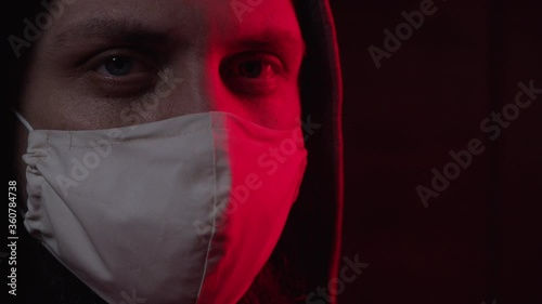 A young man in a protective mask symbolizes protection from coronavirus. A man in a hood looks into the camera, close-up