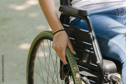 View of the wheel of a wheelchair with a female hand resting on it. Disability and healthcare concept.