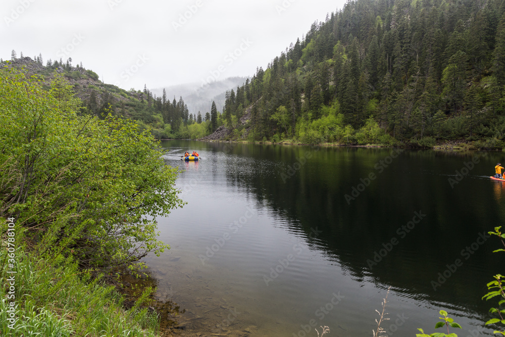 Landscape with a beautiful mountain lake among the mountains covered with coniferous and deciduous trees. An inflatable boat is floating on the lake