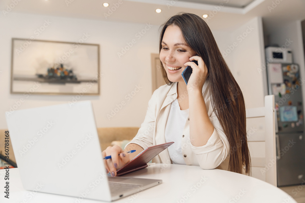 Young woman with baby speaks by phone and working with laptop on kitchen. Business Quarantine Concept Young woman with baby speaks by phone and working with laptop on kitchen. Business Quarantine Concept