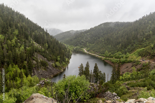 Landscape with a beautiful mountain lake among mountains and fog covered with coniferous and deciduous trees forest.