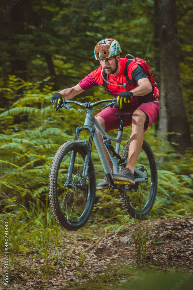 Side view of young caucasian male jumping with a mountain bike over a jump on a singletrail. Epic ride with a modern mountain bike on a trail park.