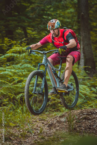 Side view of young caucasian male jumping with a mountain bike over a jump on a singletrail. Epic ride with a modern mountain bike on a trail park.