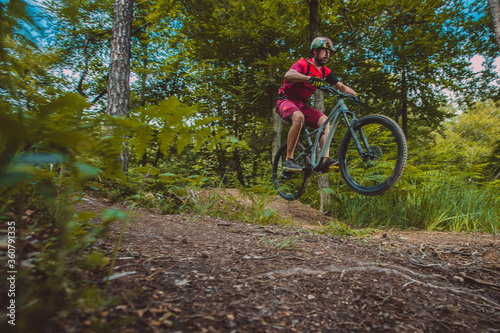 side view of young caucasian male jumping with a mountain bike over a jump on a singletrail. Epic ride with a modern mountain bike on a trail park.