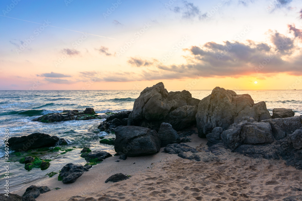 idyllic sunrise on the ocean shore. waves crashing rocks on sandy beach. beautiful cloudscape above the horizon