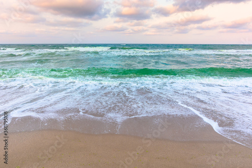 cloudy sunset sea side. waves running the sandy beach. changing windy weather in evening light