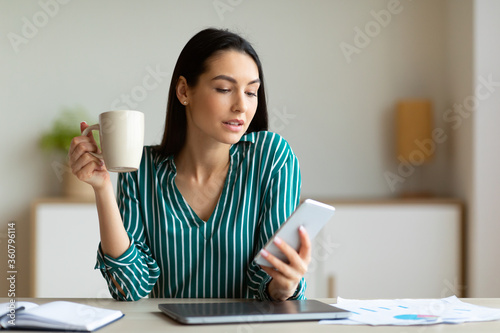 Businesswoman Using Cellphone Having Coffee Sitting In Office
