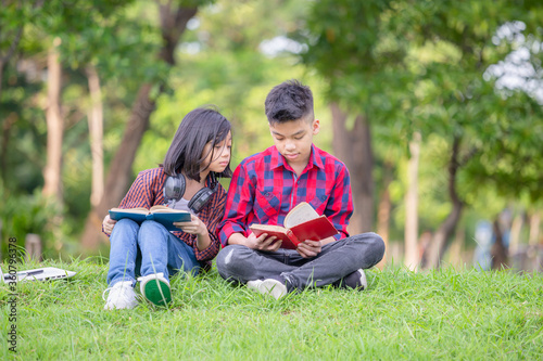 Brother and sister sitting on the grass and reading the book in the park, Kids playing & Outdoor learning concept