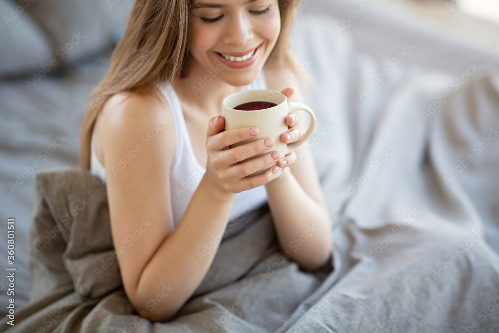 Smiling girl having cup of fresh coffee on bed in morning